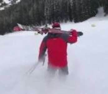 Un skieur descend une piste sur ses chaussures avec ses skis sur l'épaule