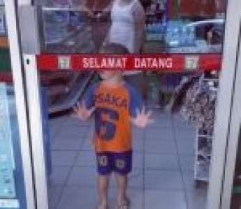 Un petit garçon pousse une porte vitrée pour sortir d’un magasin