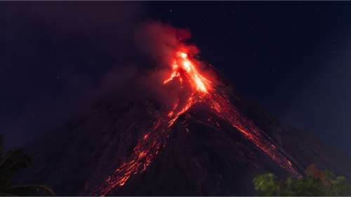 Un homme prend en photo un volcan en éruption depuis sa chambre d’hôtel