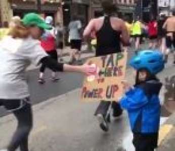 Un enfant redonne de l’énergie à des marathoniens avec une pancarte « Tap here to power up » (États-Unis)